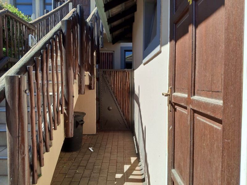 A side walkway featuring a timber staircase with balustrade, paved flooring, and a secure metal gate leading to the rear of the townhouse.