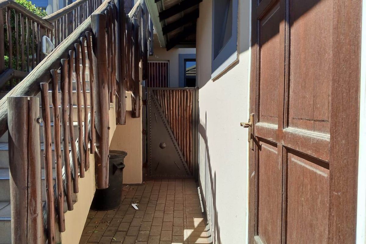 A side walkway featuring a timber staircase with balustrade, paved flooring, and a secure metal gate leading to the rear of the townhouse.