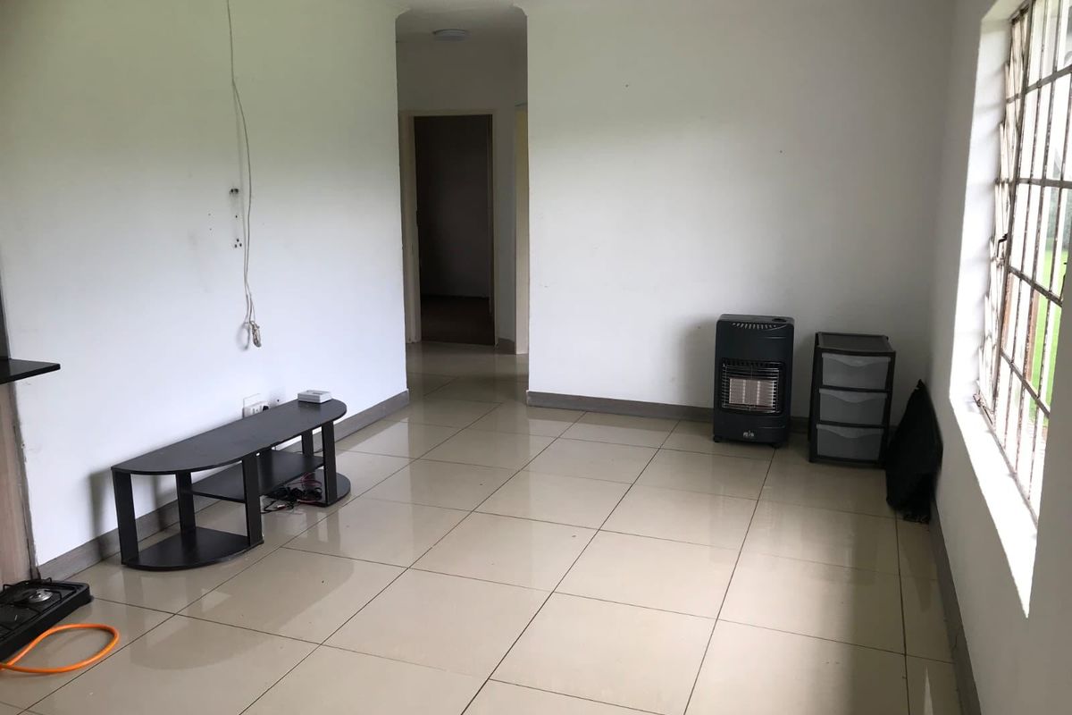 A sparsely furnished living room featuring tiled flooring and security bars on the window, presenting a blank canvas for potential interior design updates.