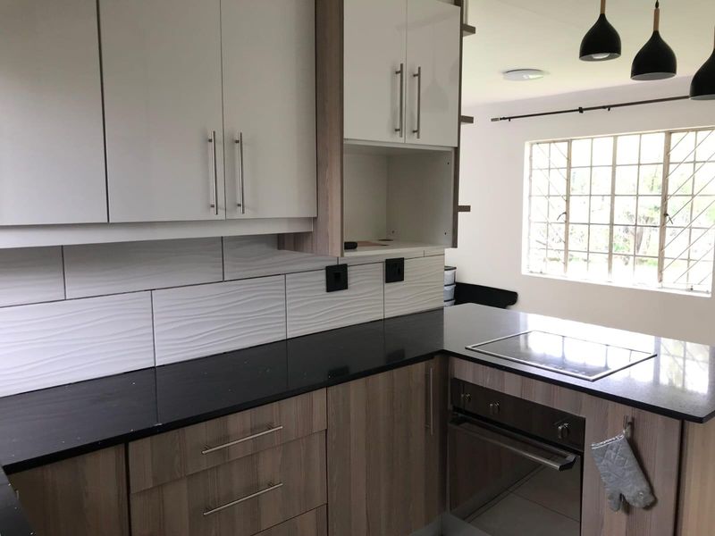 Modern kitchen featuring wood-grain and white cabinetry, black stone countertops, built-in oven, and electric hob with a textured tile backsplash.
