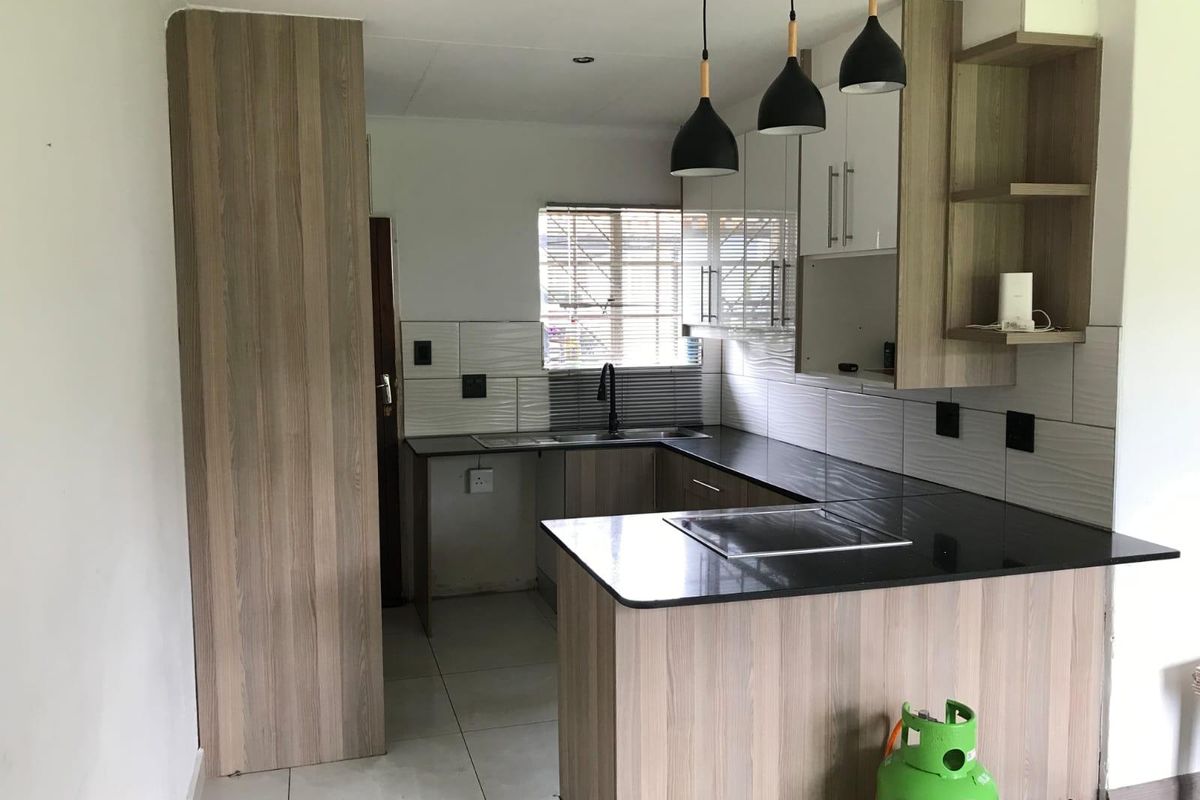 Modern kitchen featuring wood-look cabinetry, dark countertops, tiled backsplash, and contemporary pendant lighting in an open-plan layout.