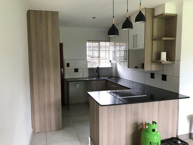 Modern kitchen featuring wood-look cabinetry, dark countertops, tiled backsplash, and contemporary pendant lighting in an open-plan layout.