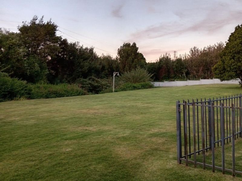 A spacious, well-maintained garden area featuring a large lawn and secure metal perimeter fencing, offering a peaceful outdoor setting.