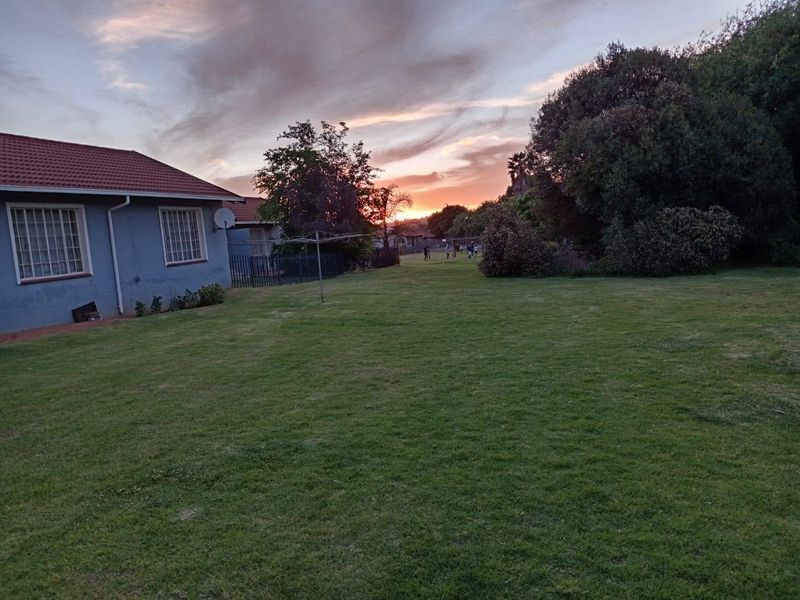 A spacious rear garden area featuring a well-maintained lawn, established trees, and a view of the side elevation of the townhouse.
