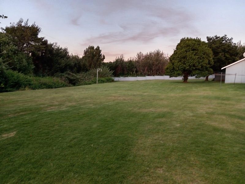 A spacious, well-maintained grass garden area featuring mature trees and perimeter fencing, providing a private outdoor space.