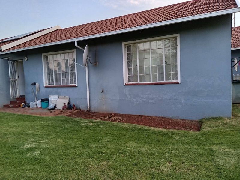 Rear view of the townhouse featuring a tiled roof, security bars on windows, and a small garden area with an external tap.