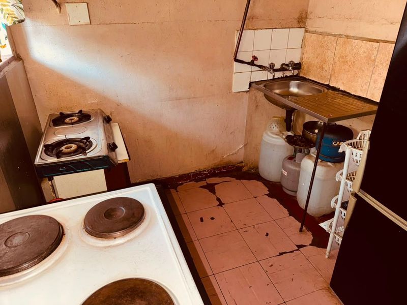 A compact kitchen area featuring a stainless steel sink, tiled splashback, and floor tiles in need of significant repair and renovation.