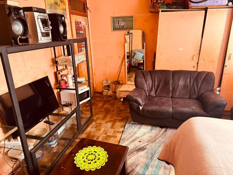 A living room area featuring parquet flooring and built-in storage, currently requiring cosmetic updates to the wall finishes and general maintenance.