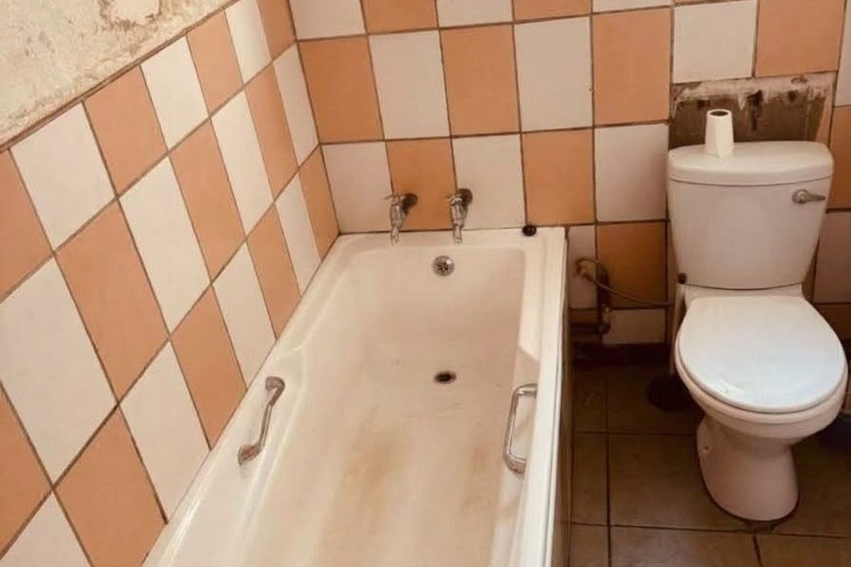 A dated bathroom featuring a bathtub and toilet, requiring significant renovation and cosmetic repairs to the wall finishes and tiling.