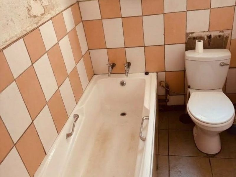 A dated bathroom featuring a bathtub and toilet, requiring significant renovation and cosmetic repairs to the wall finishes and tiling.