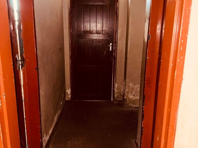 A narrow interior hallway featuring a dark timber door with a transom window, showing significant wear to the walls and door frames.