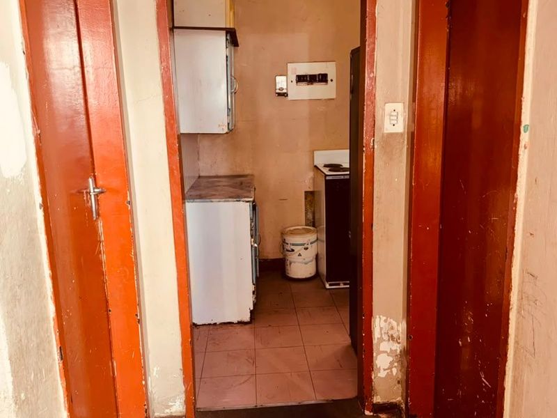 A compact, dated kitchen area featuring basic cabinetry and tiled flooring, requiring significant cosmetic updates and refurbishment to improve its functionality and aesthetic appeal.
