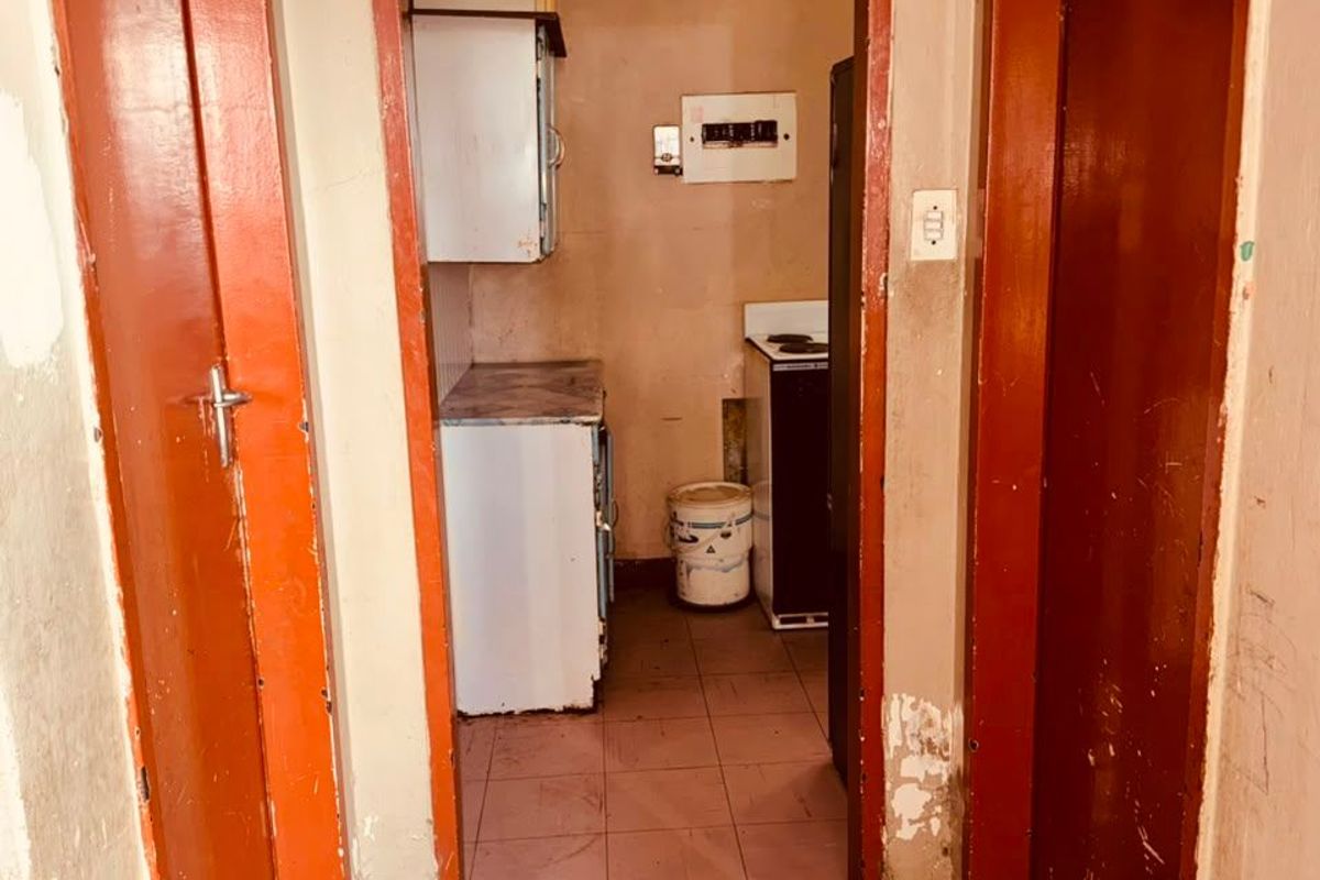 A compact, dated kitchen area featuring basic cabinetry and tiled flooring, requiring significant cosmetic updates and refurbishment to improve its functionality and aesthetic appeal.