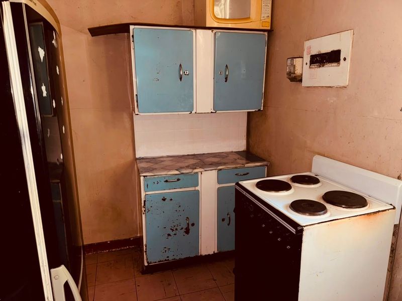 A compact kitchen featuring dated cabinetry, an electric stove, and tiled flooring, requiring significant renovation to modernize the space.