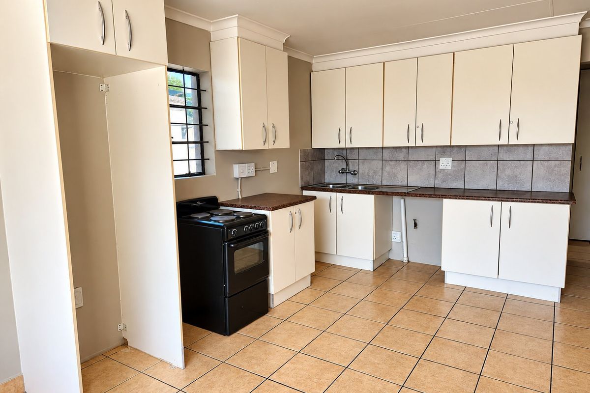 A functional kitchen featuring cream cabinetry, laminate countertops, tiled backsplash, and tiled flooring, equipped with a freestanding stove and double sink.