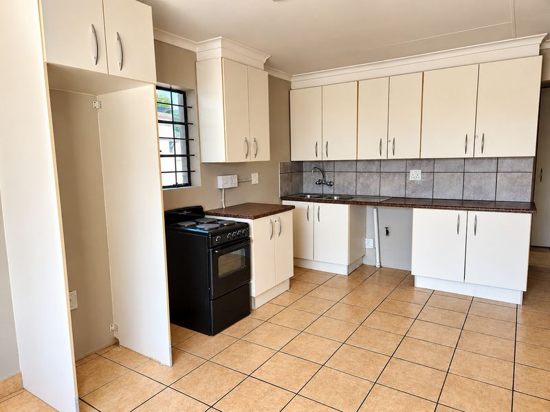A functional kitchen featuring cream cabinetry, laminate countertops, tiled backsplash, and tiled flooring, equipped with a freestanding stove and double sink.
