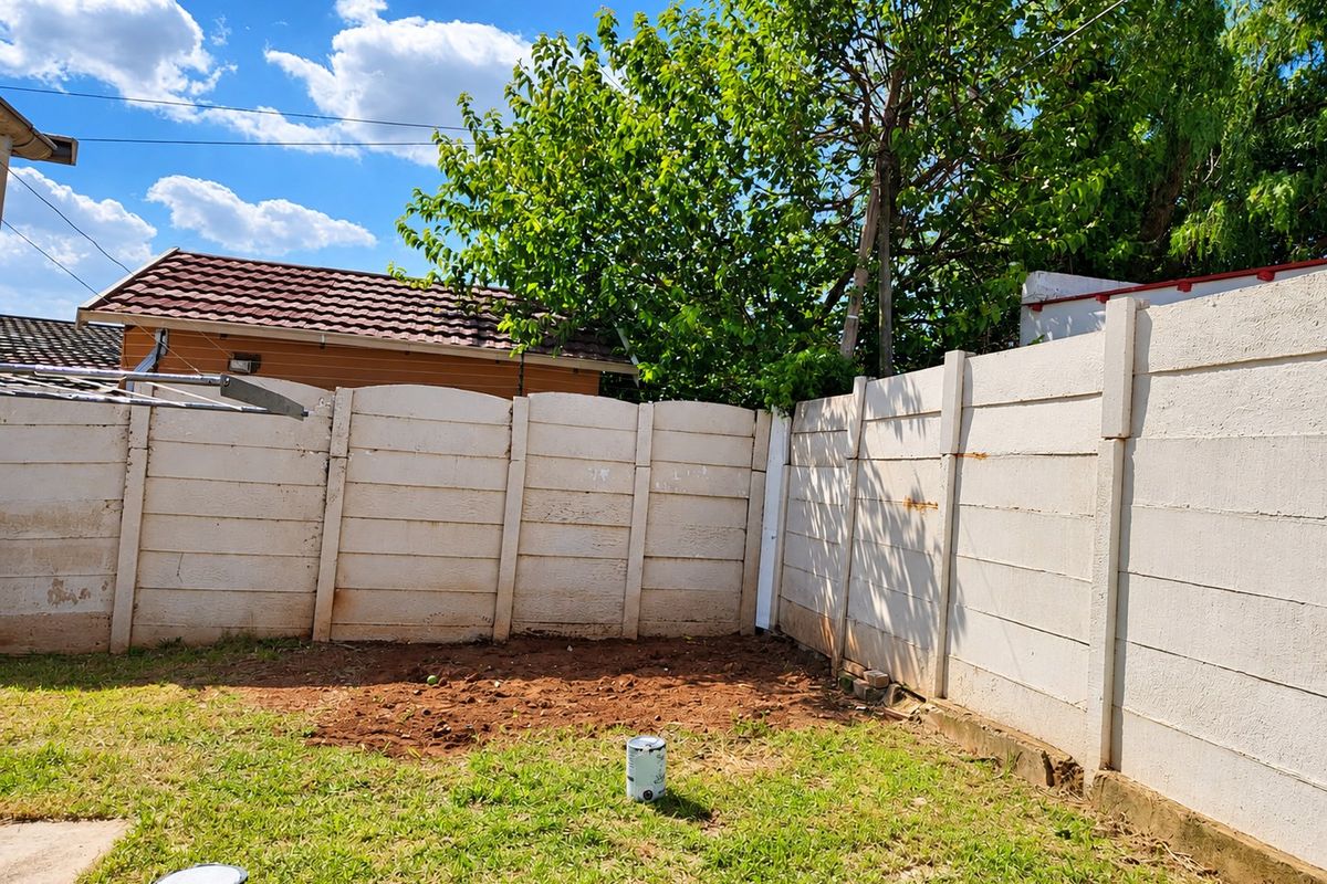 A rear garden area featuring a precast concrete boundary wall and a patch of exposed soil, offering potential for landscaping and outdoor improvement.