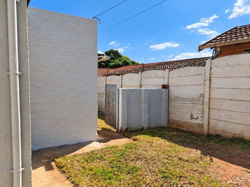 A rear exterior view of the property featuring a small lawn area, a precast concrete boundary wall, and a metal security gate.