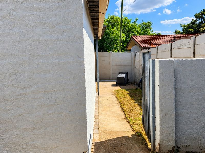 A narrow paved side path leading to the rear of the property, enclosed by concrete boundary walls and a metal gate.