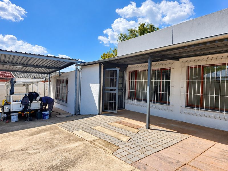 Rear exterior view of the property featuring a paved patio area, metal carport, and security bars on the windows.