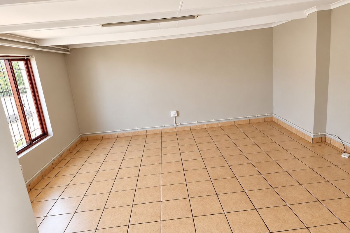 An empty living area featuring tiled flooring, exposed beam ceiling, and visible surface-mounted electrical conduit along the walls.