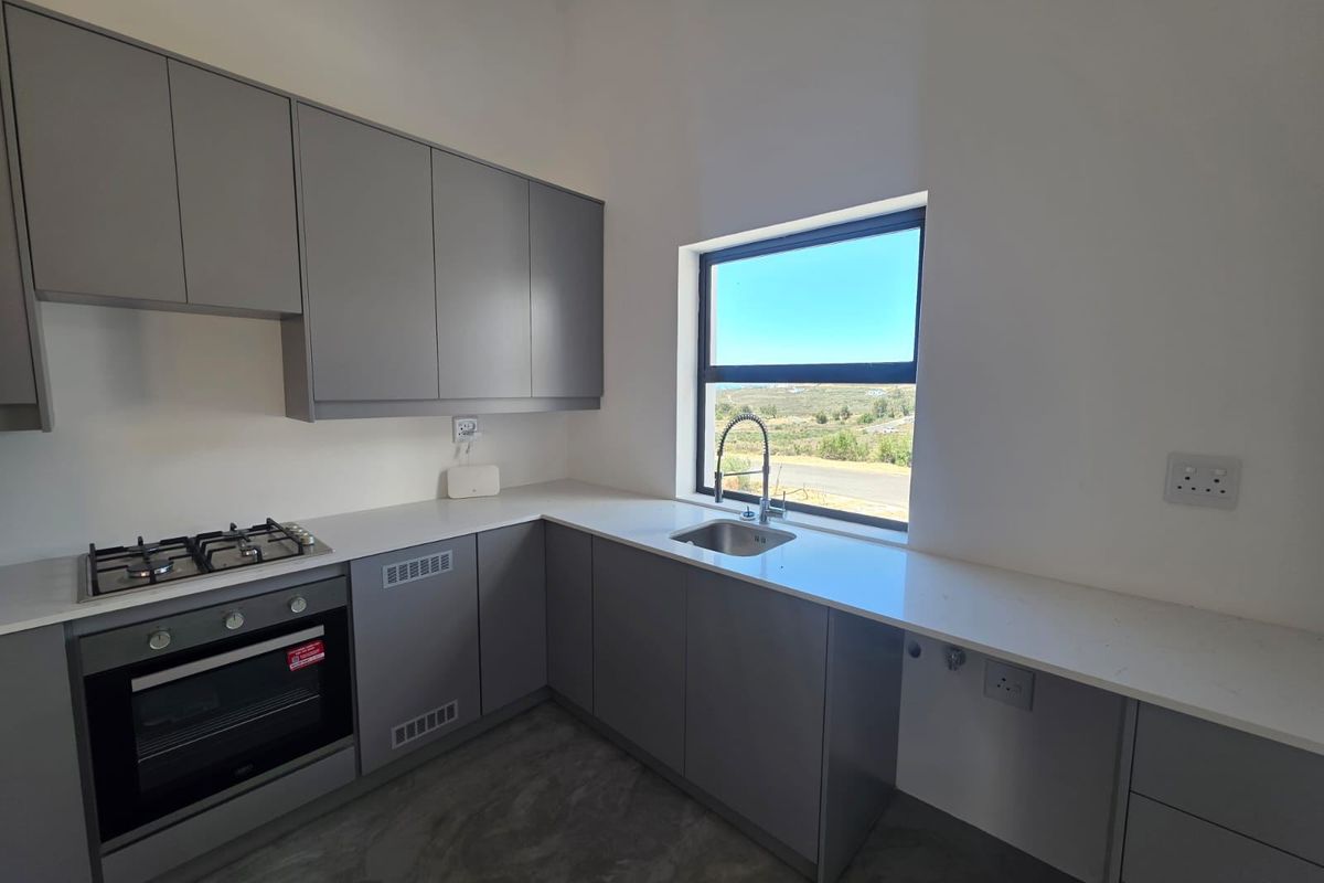 Modern kitchen featuring sleek grey cabinetry, stone countertops, a gas hob, built-in oven, and polished concrete flooring with a scenic window view.