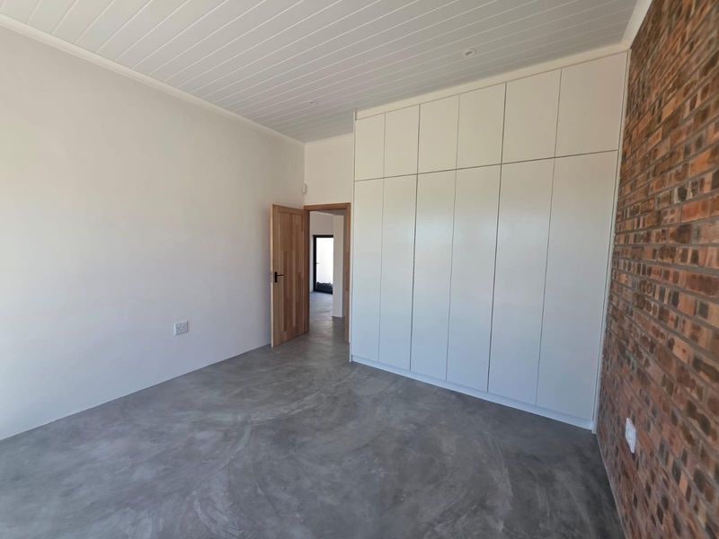 A modern, minimalist bedroom featuring polished concrete floors, an exposed brick feature wall, and extensive floor-to-ceiling built-in cabinetry.