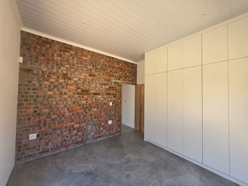 A modern bedroom featuring an exposed brick wall, polished concrete floors, and extensive built-in floor-to-ceiling cabinetry with a clean, minimalist aesthetic.