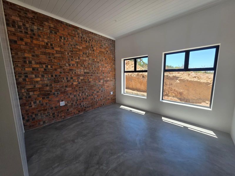 A bright, modern bedroom featuring a striking exposed brick wall, polished concrete floors, and a clean white tongue and groove ceiling.