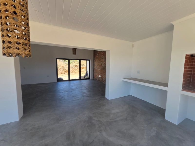 Spacious open-plan living area featuring polished concrete floors, an exposed brick feature wall, a built-in fireplace, and large sliding doors leading outdoors.