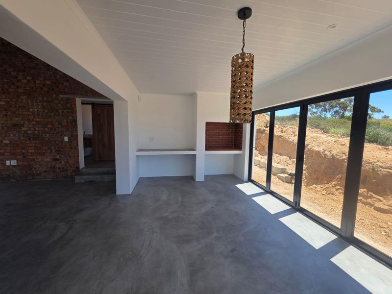 An open-plan indoor patio area featuring polished concrete floors, a built-in braai, and large bi-fold doors opening to the exterior.