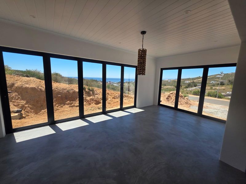 Spacious living area featuring polished concrete floors, tongue and groove ceiling, and expansive black aluminium stacker doors offering panoramic coastal views.