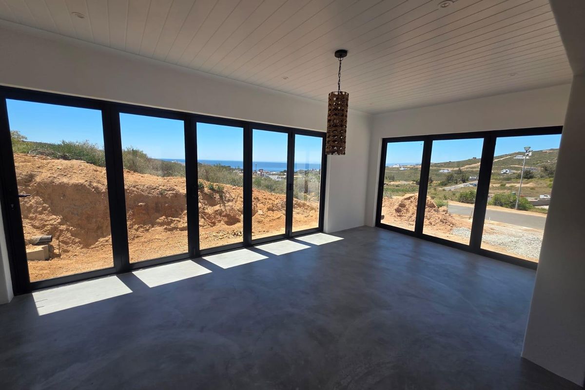 Spacious living area featuring polished concrete floors, tongue and groove ceiling, and expansive black aluminium stacker doors offering panoramic coastal views.
