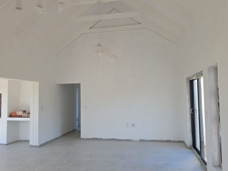 Spacious open-plan living area featuring a high vaulted ceiling with exposed rafters, tiled flooring, and a built-in fireplace, currently in an unfinished state.