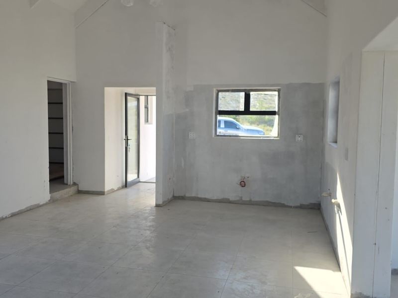 An unfinished open-plan living area featuring vaulted ceilings, tiled flooring, and aluminium window frames, currently awaiting final wall finishes and interior detailing.