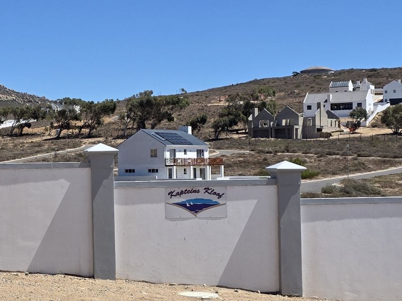 View of the Kapteins Kloof estate entrance featuring a boundary wall and a residential house with solar panels in the background.
