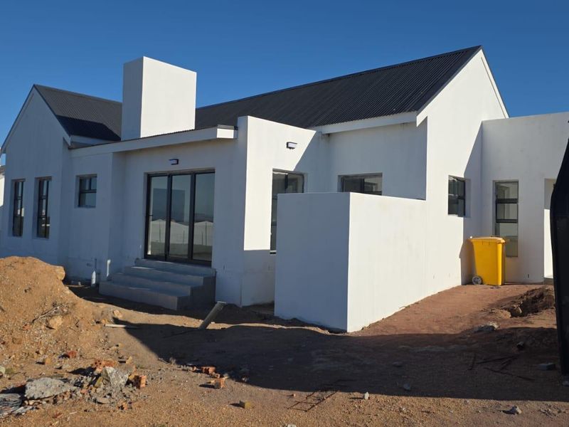 Rear view of a modern white house with a corrugated metal roof, sliding glass doors, and unfinished surrounding landscaping.