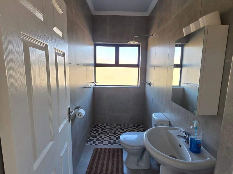 A compact, modern bathroom featuring tiled walls and flooring, a pedestal basin, and a shower area with a window for natural light.