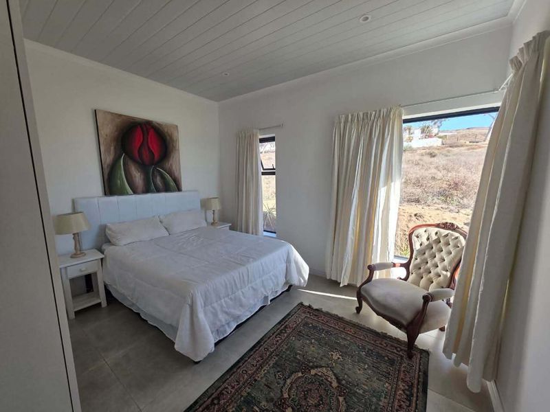 A bright and well-maintained bedroom featuring tiled flooring, a clean tongue and groove ceiling, and large windows providing natural light and exterior views.