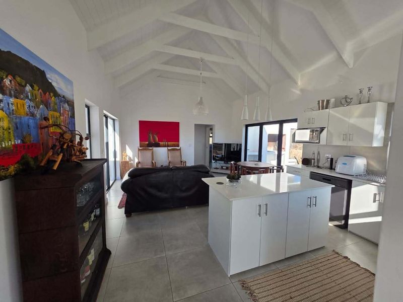 Spacious open-plan living area featuring a modern kitchen with a central island, vaulted ceilings with exposed beams, and large sliding doors leading outdoors.