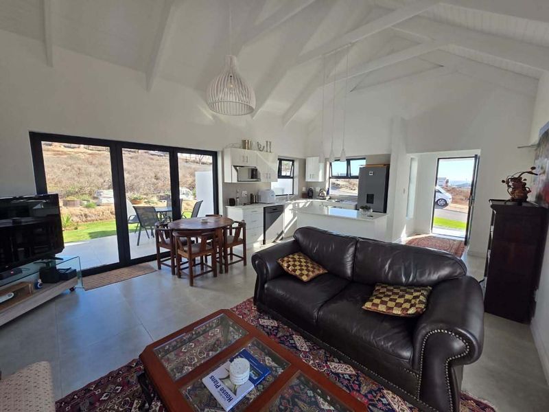 Spacious open-plan living area featuring a vaulted ceiling with exposed rafters, modern kitchen with island, and large bi-fold doors opening to the outdoor patio.