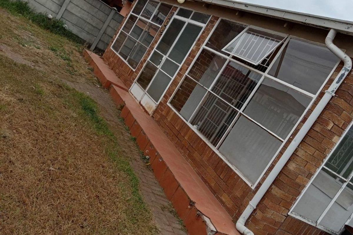 Rear exterior view of the house featuring a brick facade, large windows with security bars, and a concrete patio area leading to the garden.