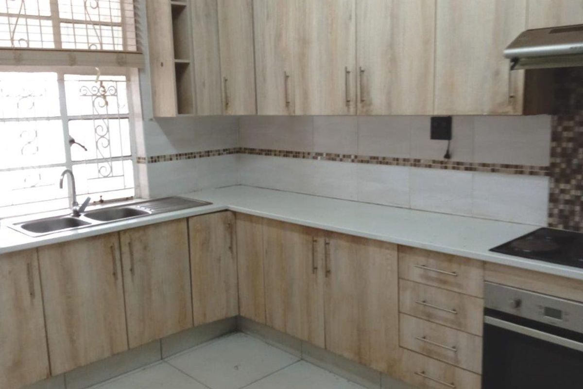 A functional kitchen featuring light wood-look cabinetry, stone-style countertops, a built-in oven, and a stainless steel sink with a window view.
