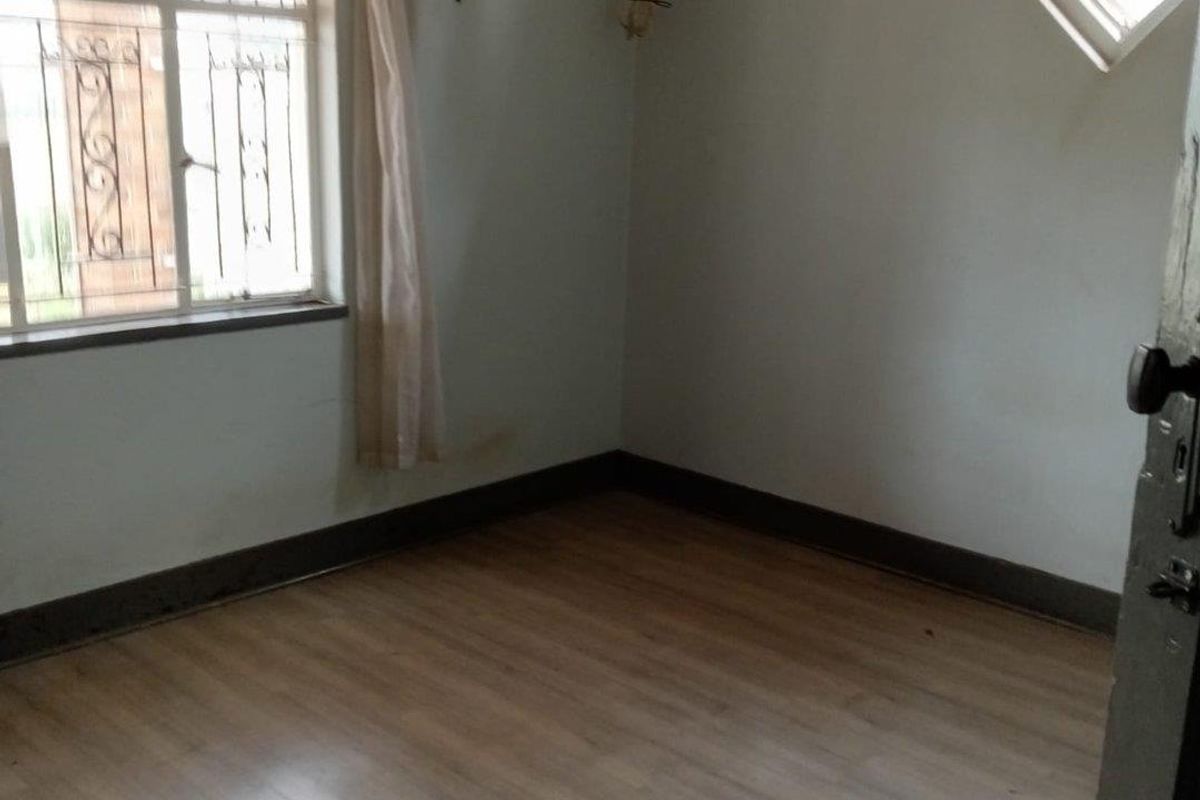 An empty bedroom featuring light wood-look flooring, a large window with security bars, and a small diamond-shaped accent window.