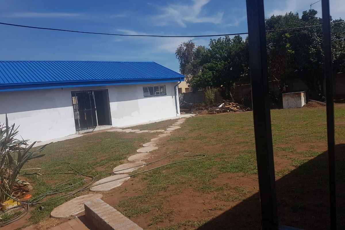 A view of the rear garden featuring a lawn, stone pathway, and the rear elevation of the house with a blue metal roof.