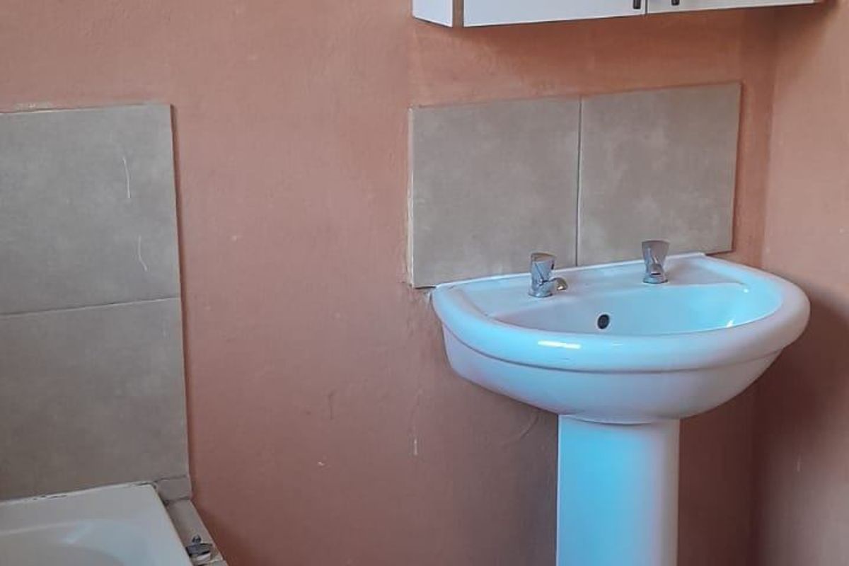 A functional bathroom featuring a pedestal basin, built-in bathtub, and wall-mounted storage cabinet with tiled splashbacks and flooring.