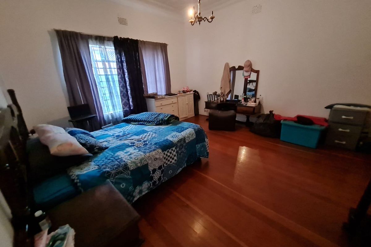 Spacious bedroom featuring polished hardwood flooring, decorative ceiling rose, and large windows with security bars.