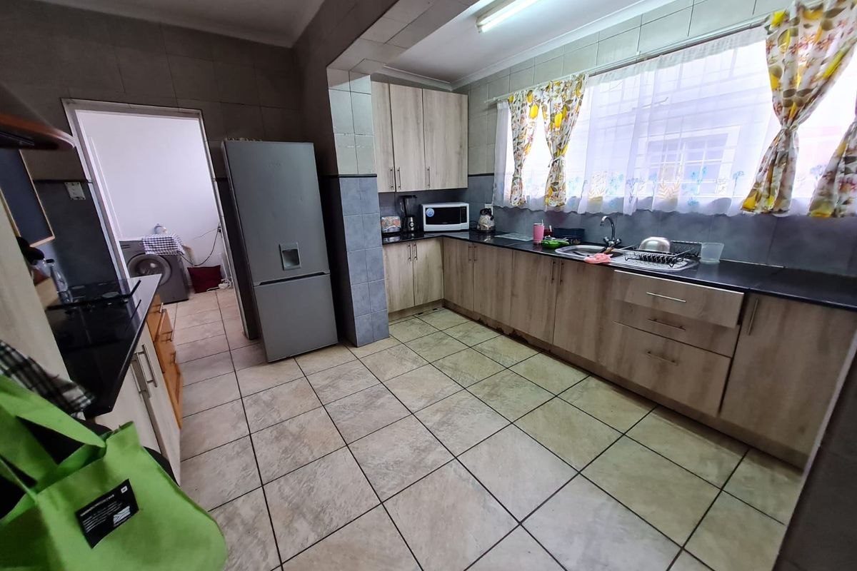 Functional kitchen featuring laminate cabinetry, granite countertops, and tiled flooring, with an adjacent laundry area visible through the doorway.