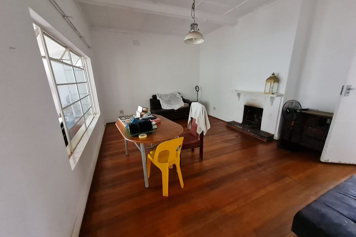 A living room featuring original hardwood flooring, a traditional fireplace with a mantelpiece, and large steel-framed windows providing natural light.