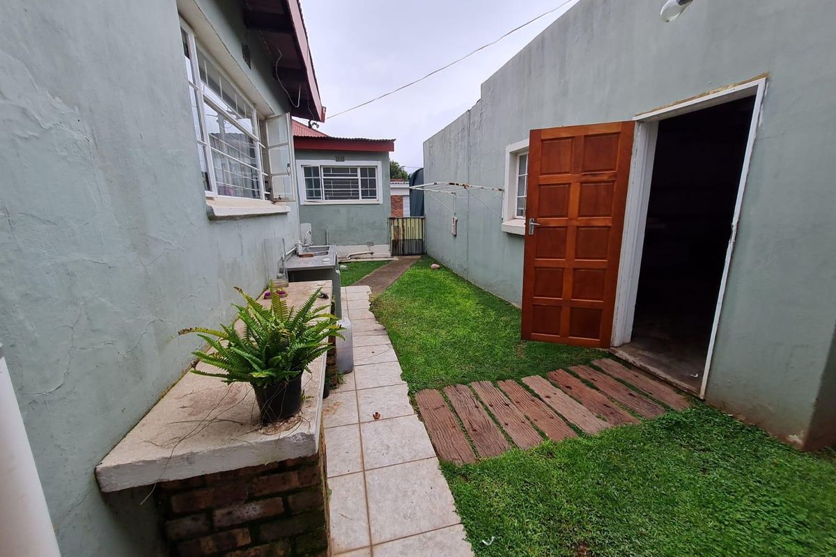 Rear exterior view of the townhouse featuring a small garden, tiled pathway, outdoor sink, and access to a secondary structure via a timber door.